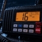 Radio VHF marina de noche con el canal 16 en pantalla y el botón de socorro DISTRESS con la tapa levantada