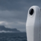 Balise EPIRB installée sur son support au bastingage d’un navire, avec la mer et la côte en arrière-plan